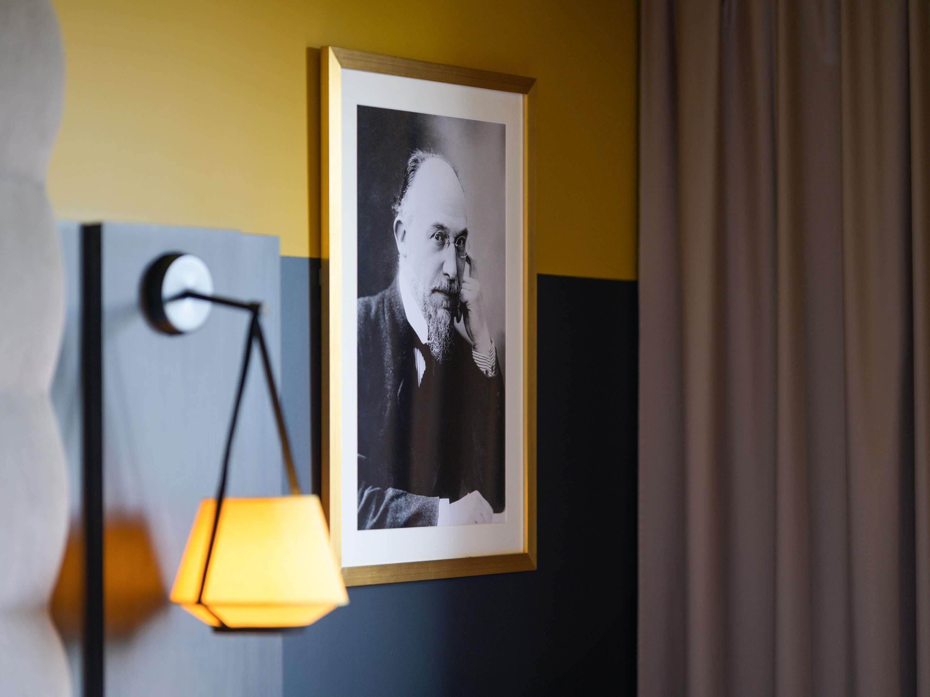 A framed portrait on a wall, a lamp, and a curtain.