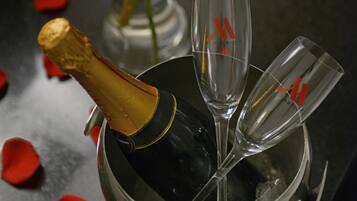A bottle of champagne in a bucket with two glasses and a bouquet of red roses.