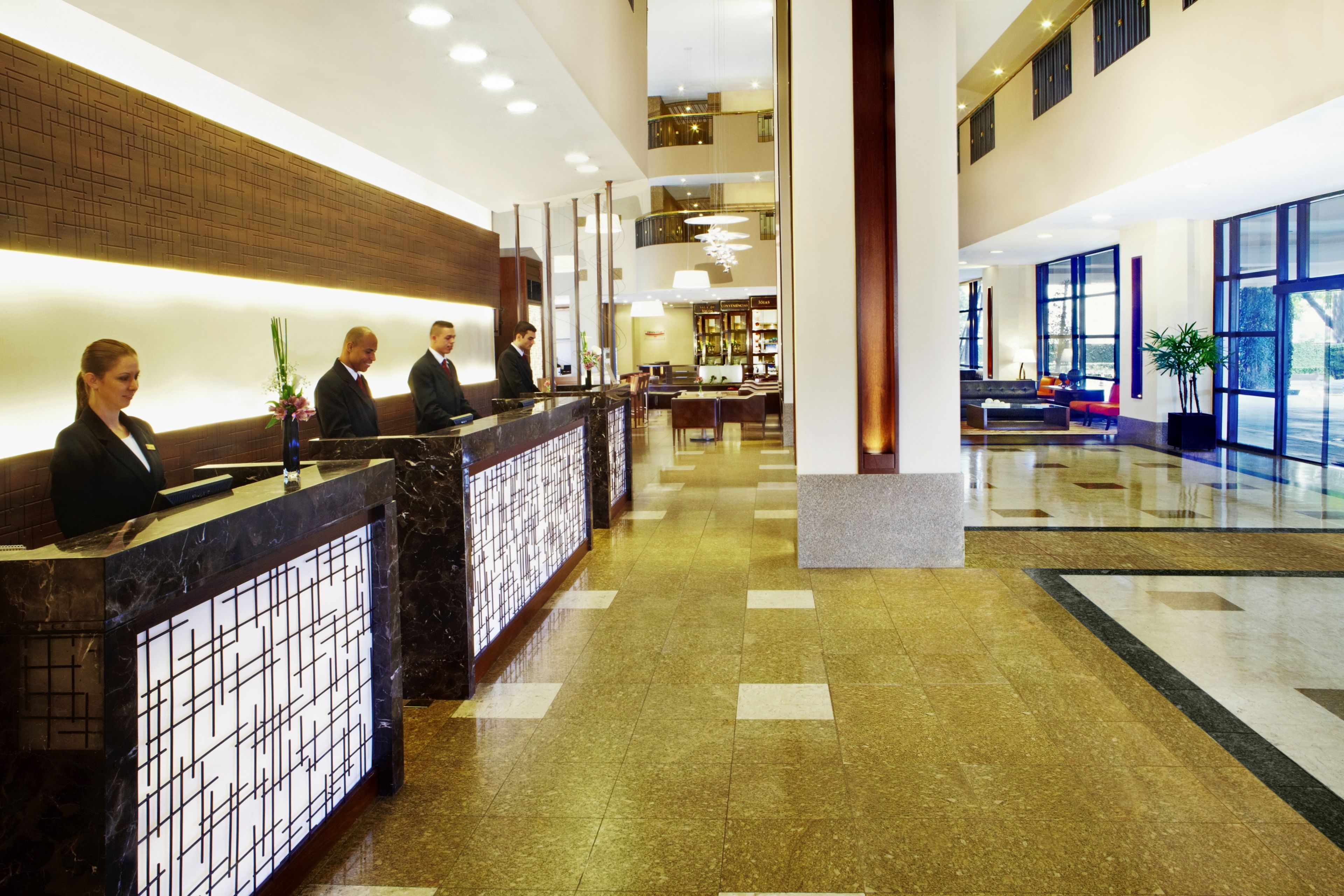 A hotel reception area with a marble counter, a seating area with sofas, and large windows offering views.