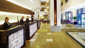 A hotel reception area with a marble counter, a seating area with sofas, and large windows offering views.