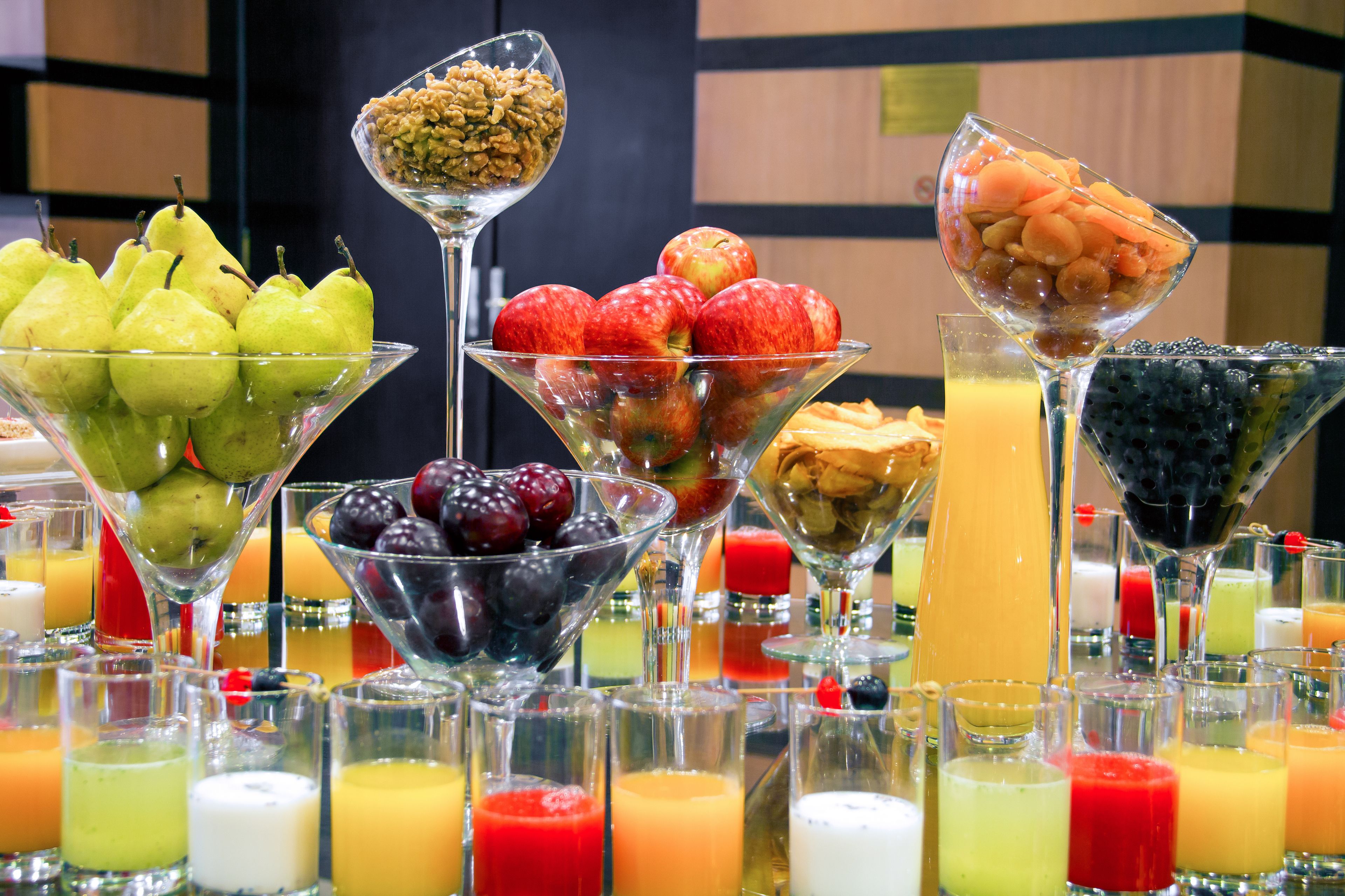 A variety of fruits and juices arranged in glass bowls and glasses, suggesting a buffet or self-serve setup.