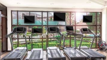 Un gimnasio con cintas de correr y bicicletas estáticas, amplias ventanas con vistas a edificios y zonas verdes.