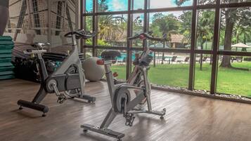 A gym with stationary bikes and exercise balls, large windows with a view of a pool and greenery.