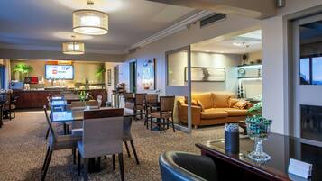 Um saguão de hotel com área de refeições, um sofá e uma TV exibindo 'CNN Highlight'.