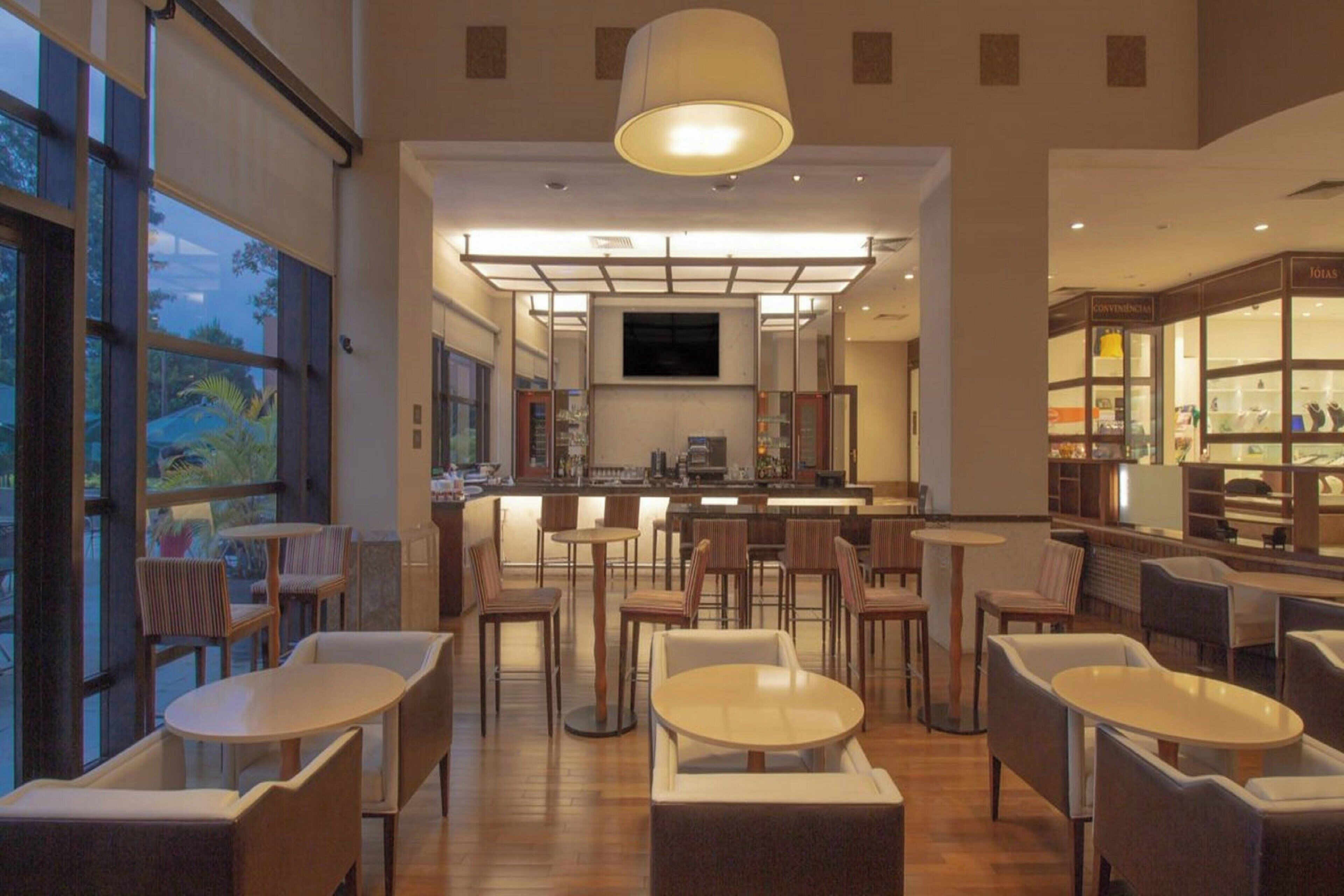 Un restaurant moderne doté d’un bar, de plusieurs types de sièges, notamment des tables et des banquettes, et d’une grande fenêtre offrant une vue panoramique.