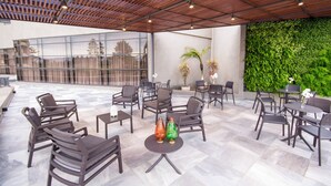 An outdoor seating area with multiple tables and chairs, a wooden ceiling, and a green wall.