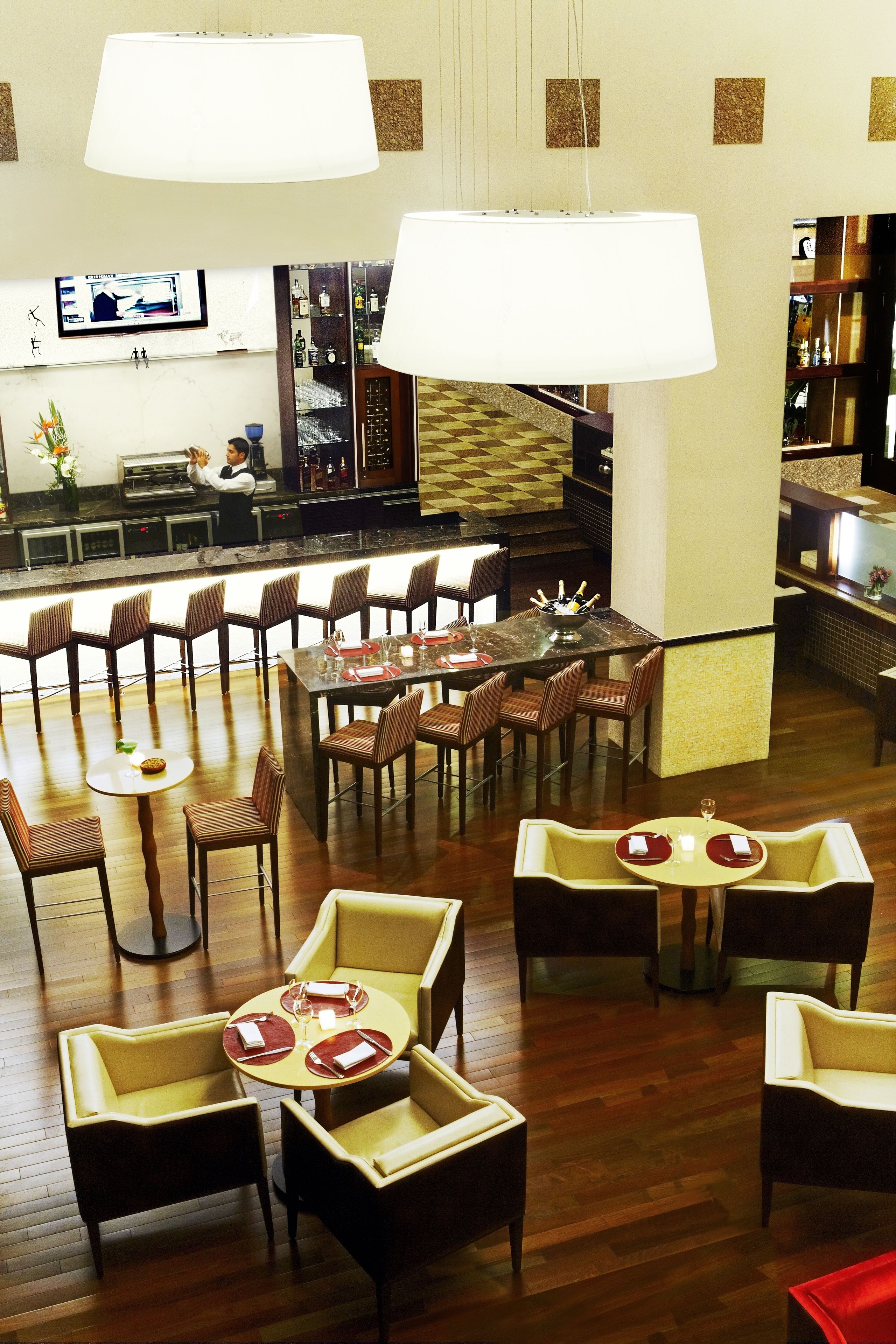 A restaurant with multiple dining areas, including a bar/lounge area with a bar counter and seating. There are several tables and chairs arranged for dining, and a television mounted on the wall.