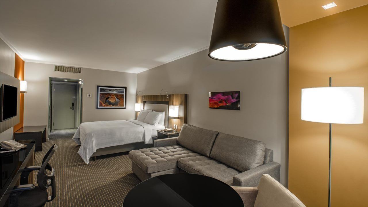 Une chambre d’hôtel comprenant un lit, un canapé, un bureau avec une chaise, une télévision et une lampe.