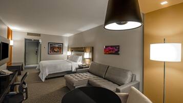 Habitación de hotel con cama, sofá, escritorio con silla, televisor y lámpara.