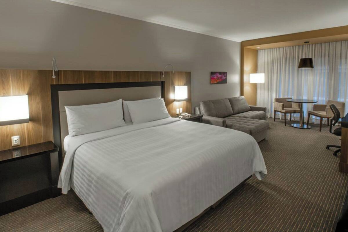 A hotel room with a large bed, a sofa, a desk with a chair, and a small table.