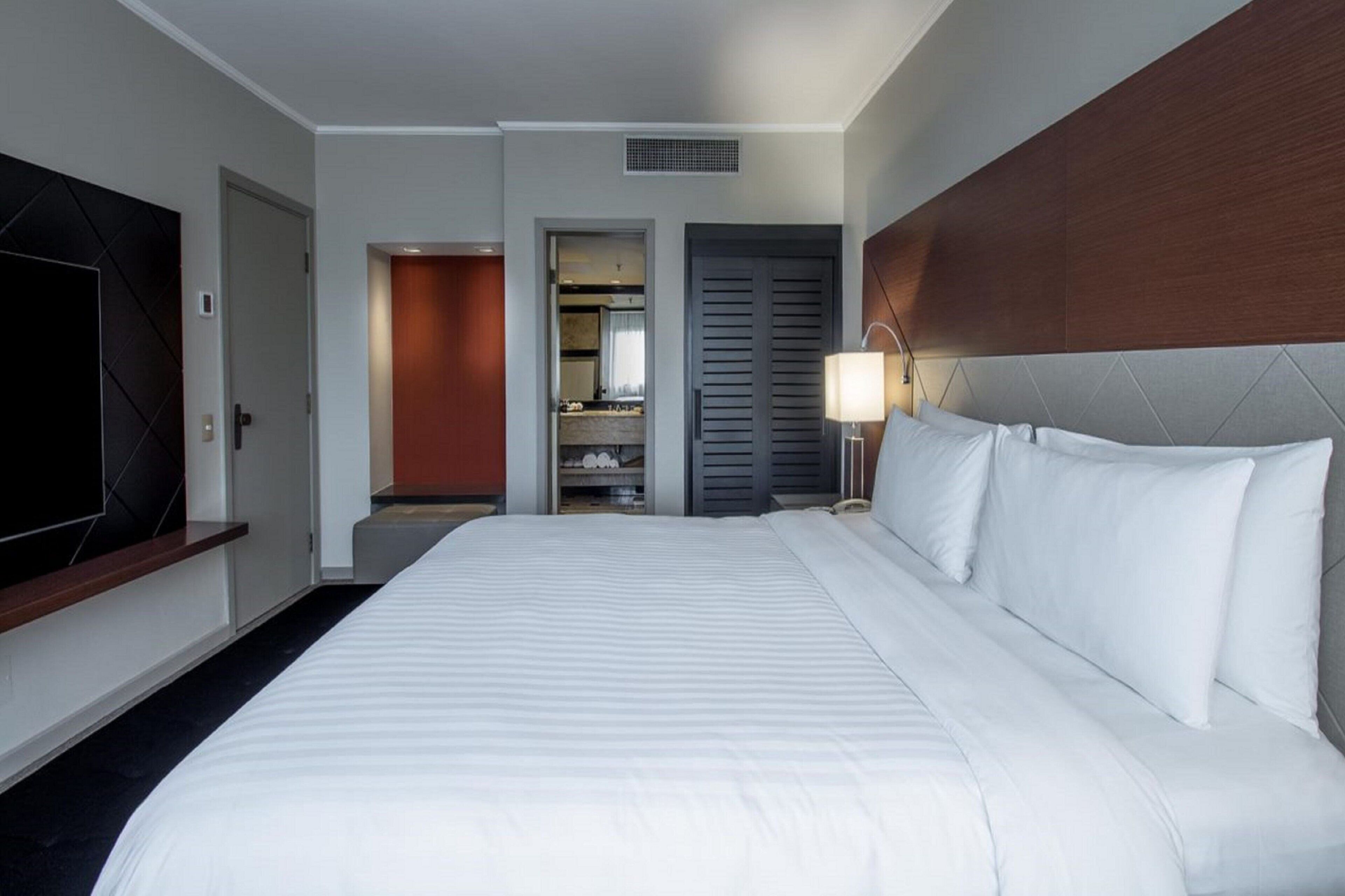 A hotel room with a large bed, a television on the wall, a wardrobe, and a bathroom visible through an open door.