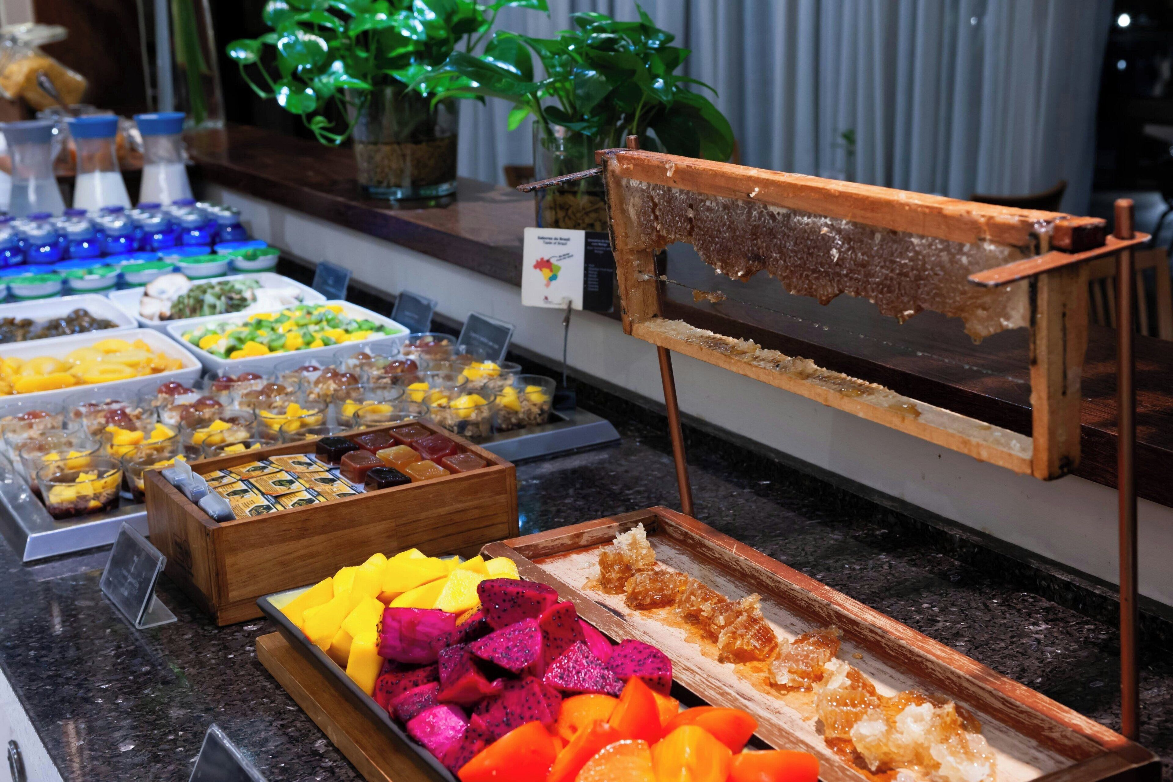 Un bufé con diversas opciones de comida, entre ellas frutas, postres y una presentación de panales de miel.