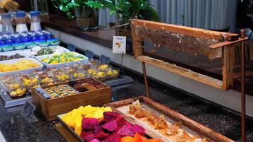 Un bufé con diversas opciones de comida, entre ellas frutas, postres y una presentación de panales de miel.