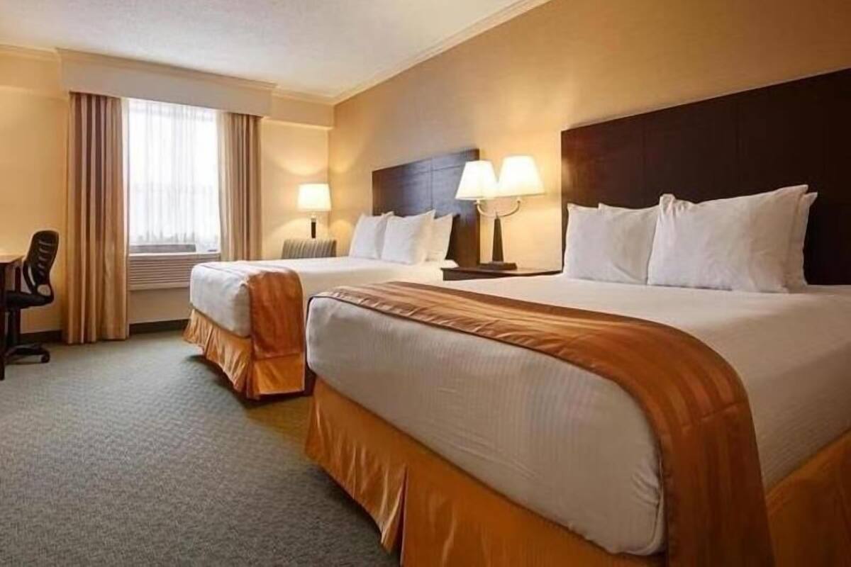 A hotel room with two beds, a desk, and a window with curtains.
