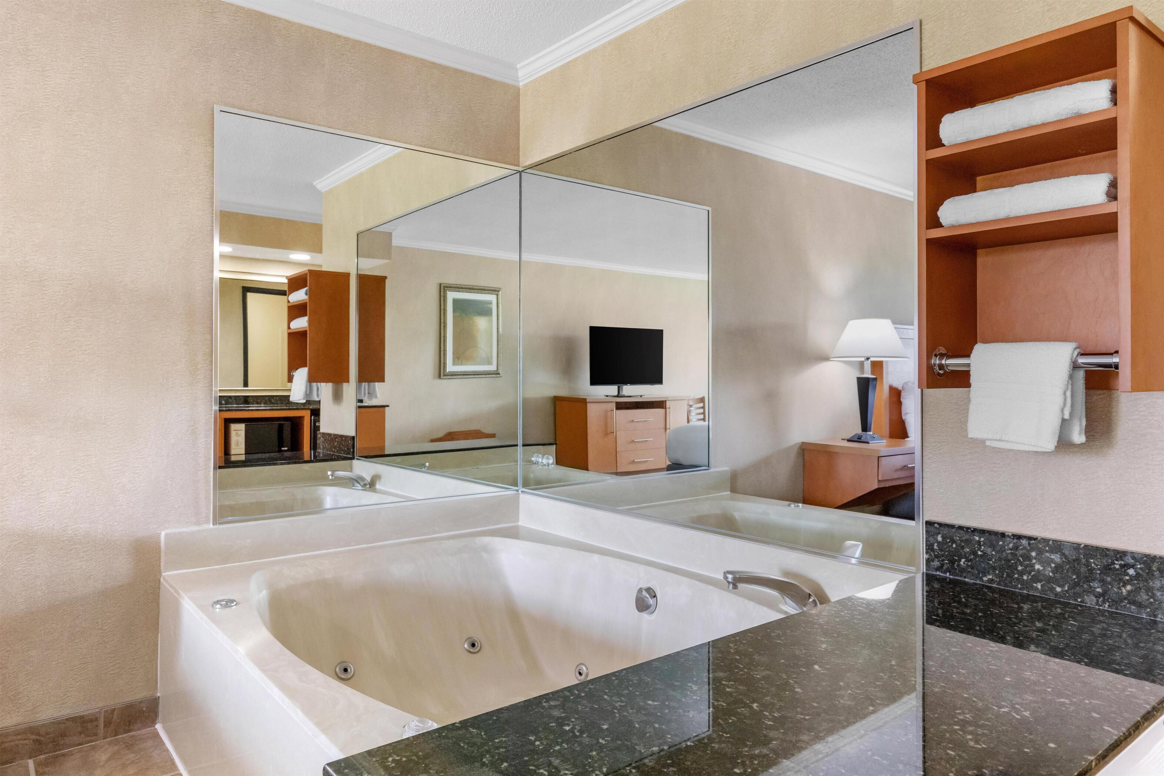 Un baño moderno con una bañera grande, una ducha con mampara de vidrio, un tocador con espejo y un estante de madera con toallas.