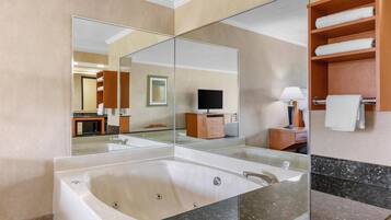 Un baño moderno con una bañera grande, una ducha con mampara de vidrio, un tocador con espejo y un estante de madera con toallas.