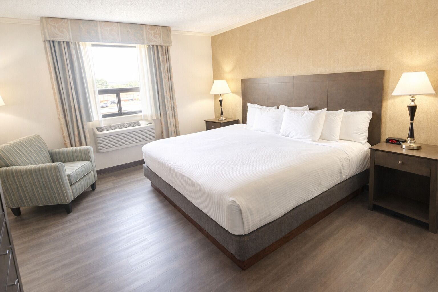 Une chambre d’hôtel avec un grand lit, deux tables de chevet, une chaise et une fenêtre avec des rideaux.