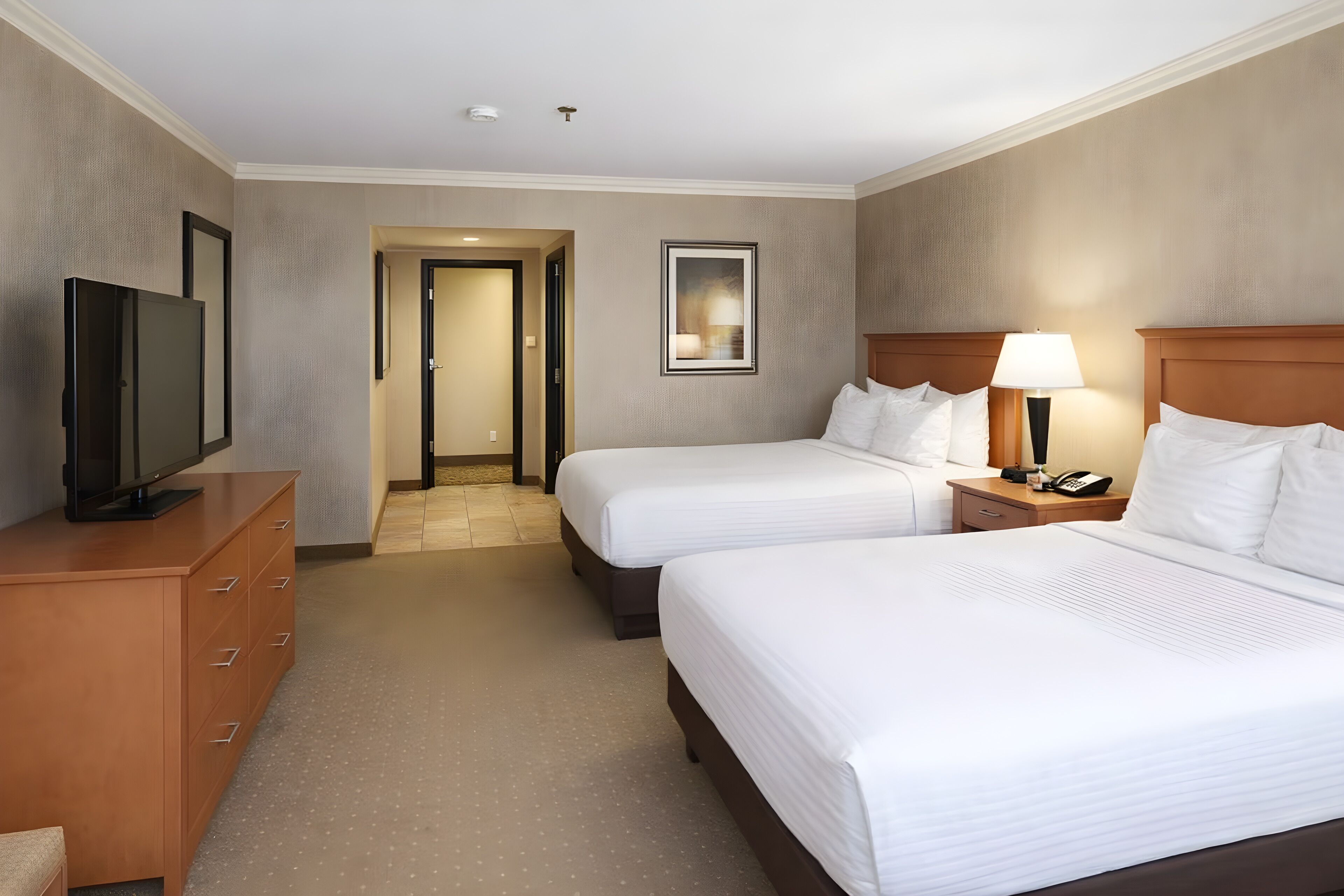 A hotel room with two beds, a TV, a desk, and a lamp.