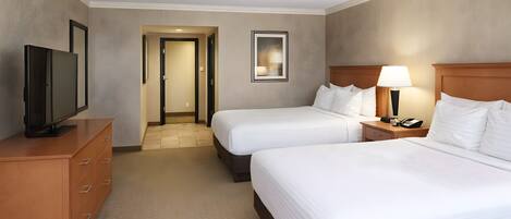 A hotel room with two beds, a TV, a desk, and a lamp.