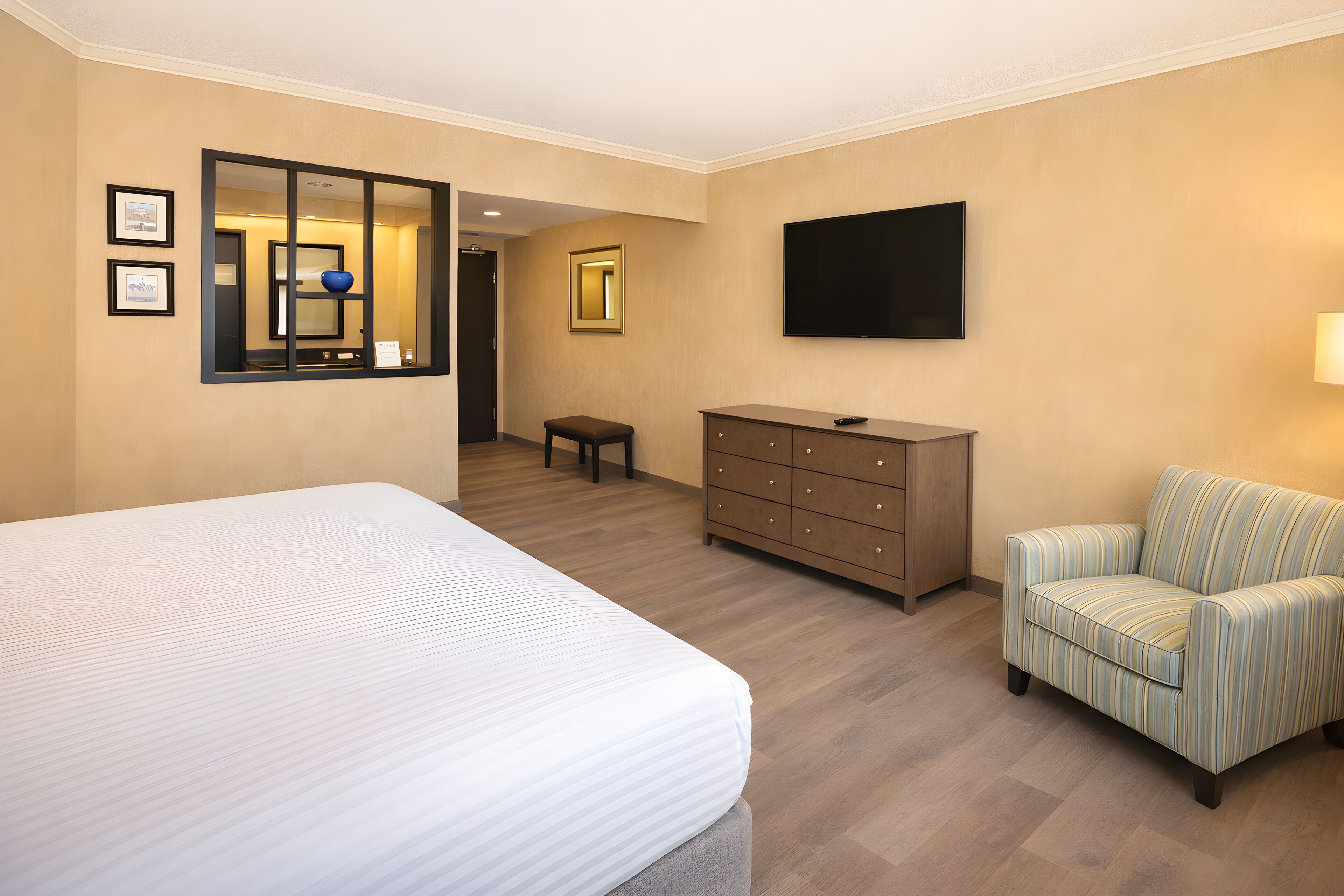 Una habitación de hotel con una cama grande, un aparador, un televisor y un sillón a rayas.