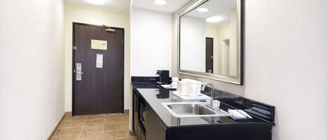 Pasillo que conduce a un baño con lavamanos, espejo y cafetera.