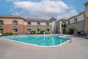A swimming pool with a curved edge, surrounded by a patio area with lounge chairs and a building with multiple windows and balconies.