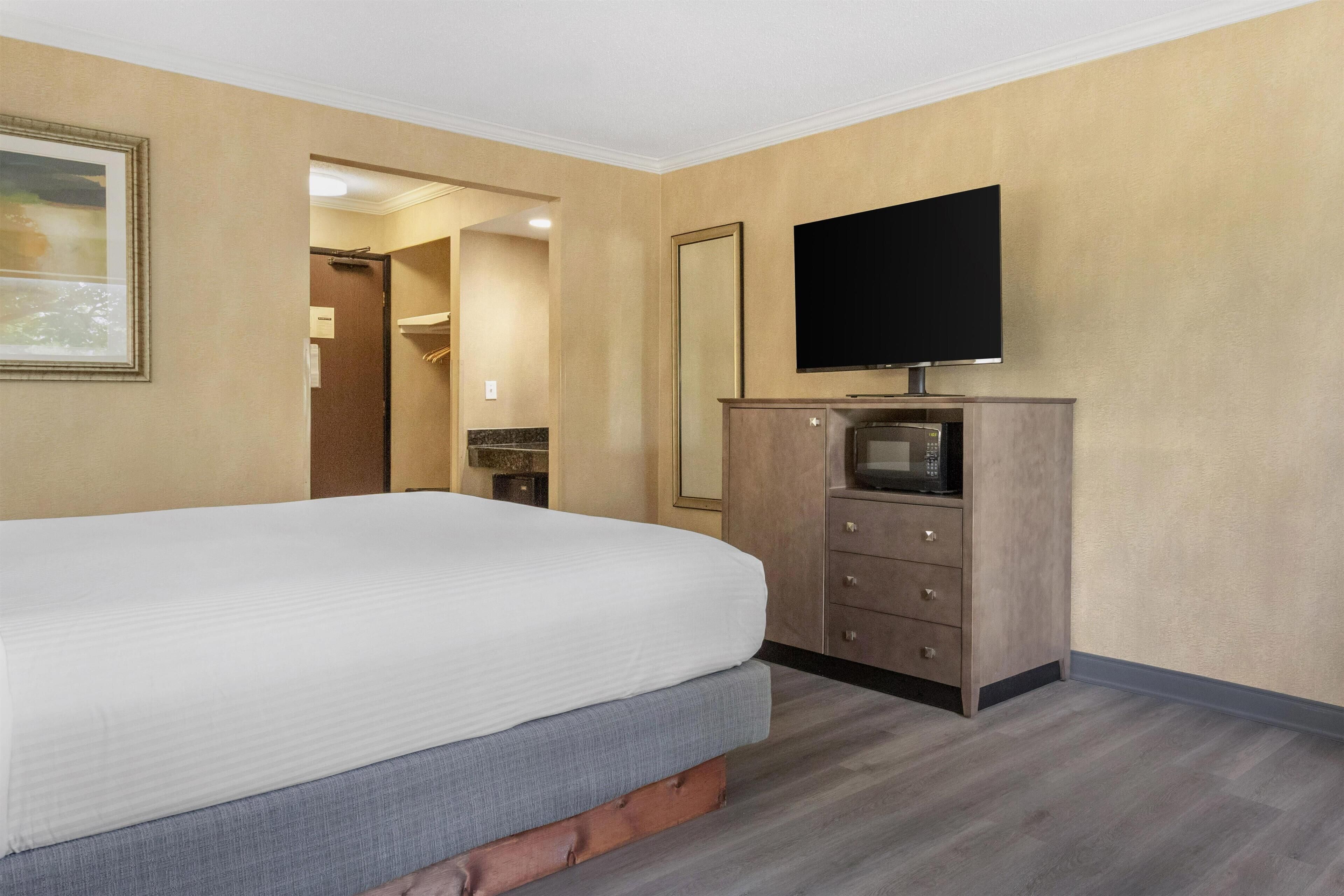A hotel room with a bed, a flat-screen TV, a wooden dresser, and a mirror.
