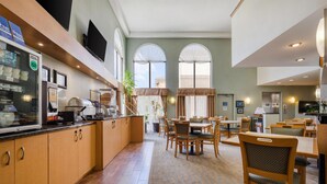 A hotel dining area with a kitchen counter, dining tables, chairs, and large windows. - Best Western Davison Inn (Davison)