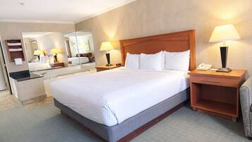 A hotel room with a large bed, two bedside tables with lamps, a mirror, a bathroom with a sink and mirror, and a small seating area with a chair.