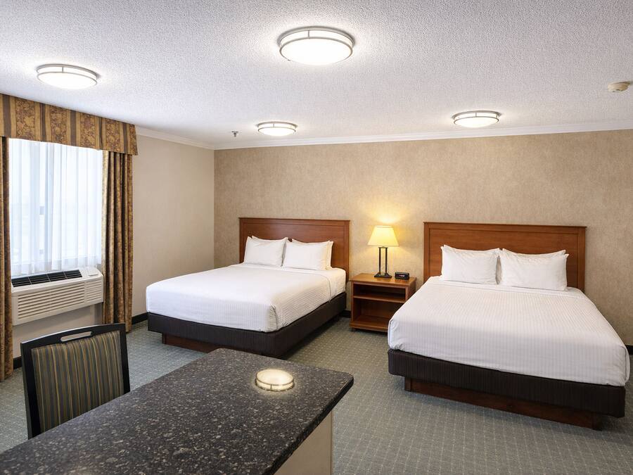 Une chambre d’hôtel avec deux lits, un bureau, une chaise, une fenêtre avec des rideaux et un plafond doté d’un éclairage encastré.
