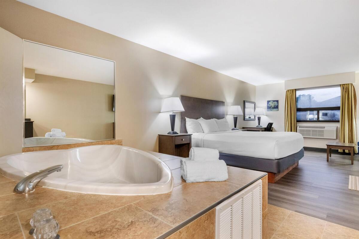 A hotel room with a large bed, a bathroom with a bathtub, a desk, and a window with curtains.