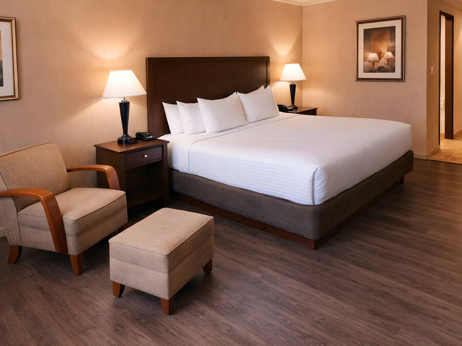 A hotel room with a large bed, two bedside tables with lamps, a chair, and an ottoman.