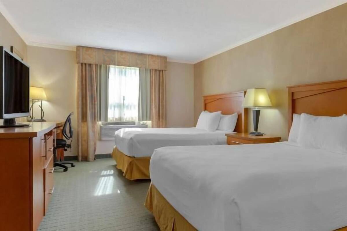 A hotel room with two beds, a desk, a television, and a window with curtains.