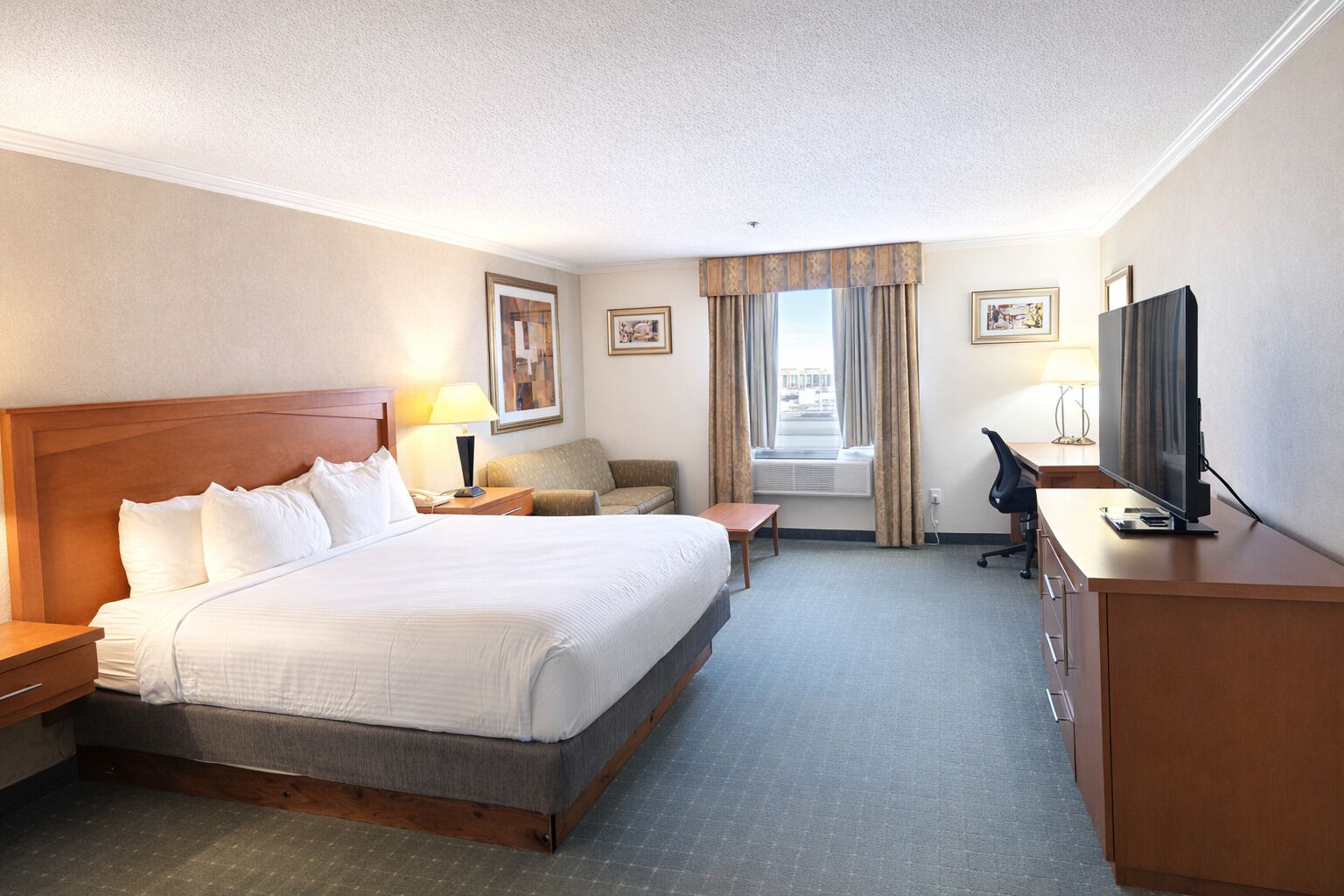 Ein Hotelzimmer mit einem großen Bett, einem Schreibtisch mit Stuhl, einem Fernseher und einem Fenster mit Vorhängen.