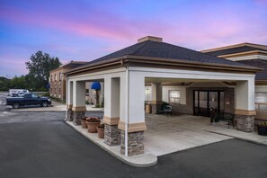 A hotel with a covered entrance, outdoor seating, and a parking lot.
