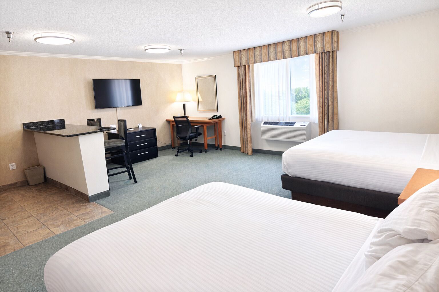 Une chambre d’hôtel avec un lit, un bureau avec un ordinateur, une télévision et une fenêtre avec des rideaux.