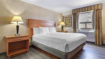 Quarto de hotel com uma cama grande, cabeceira de madeira, duas mesas de cabeceira com luminárias, um criado-mudo e uma janela com cortinas.
