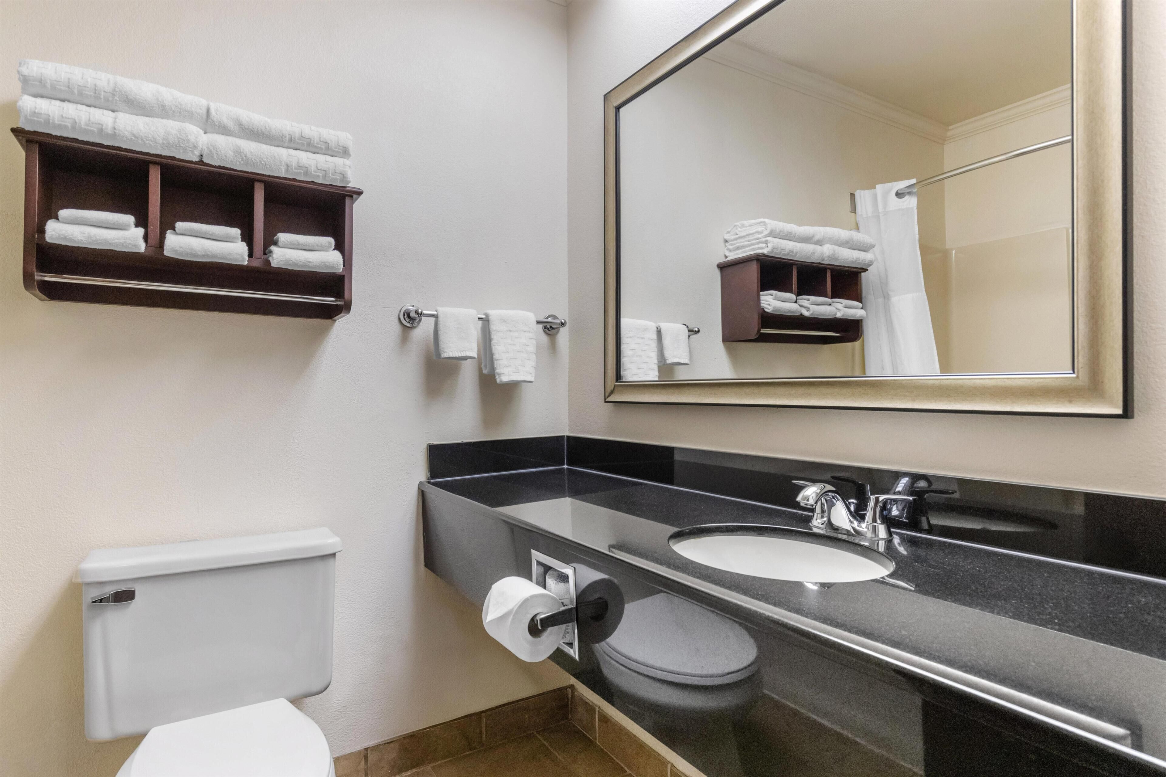 A bathroom with a toilet, sink, mirror, towel rack, and a shelf with folded towels.