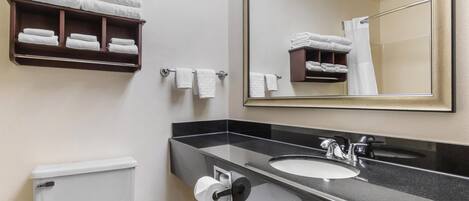 Une salle de bain comprenant des toilettes, un lavabo, un miroir, un porte-serviettes et une étagère avec des serviettes pliées.