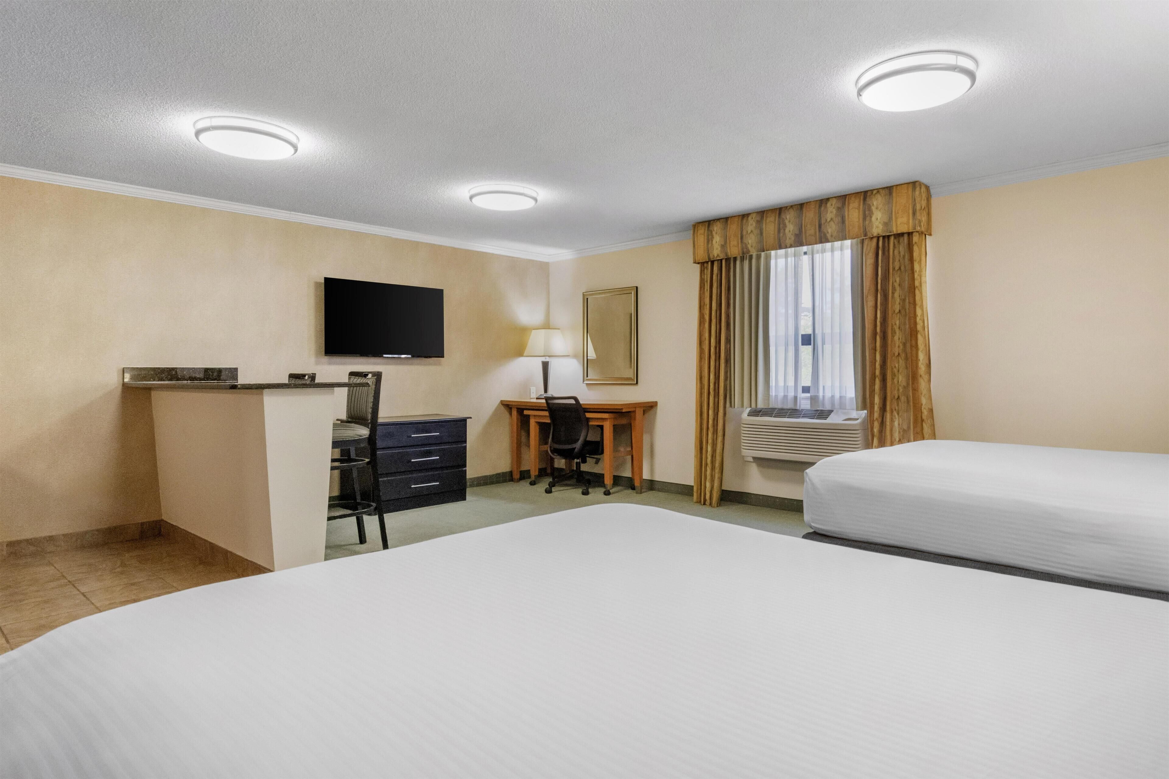 A hotel room with a bed, desk, chair, TV, and window with curtains.