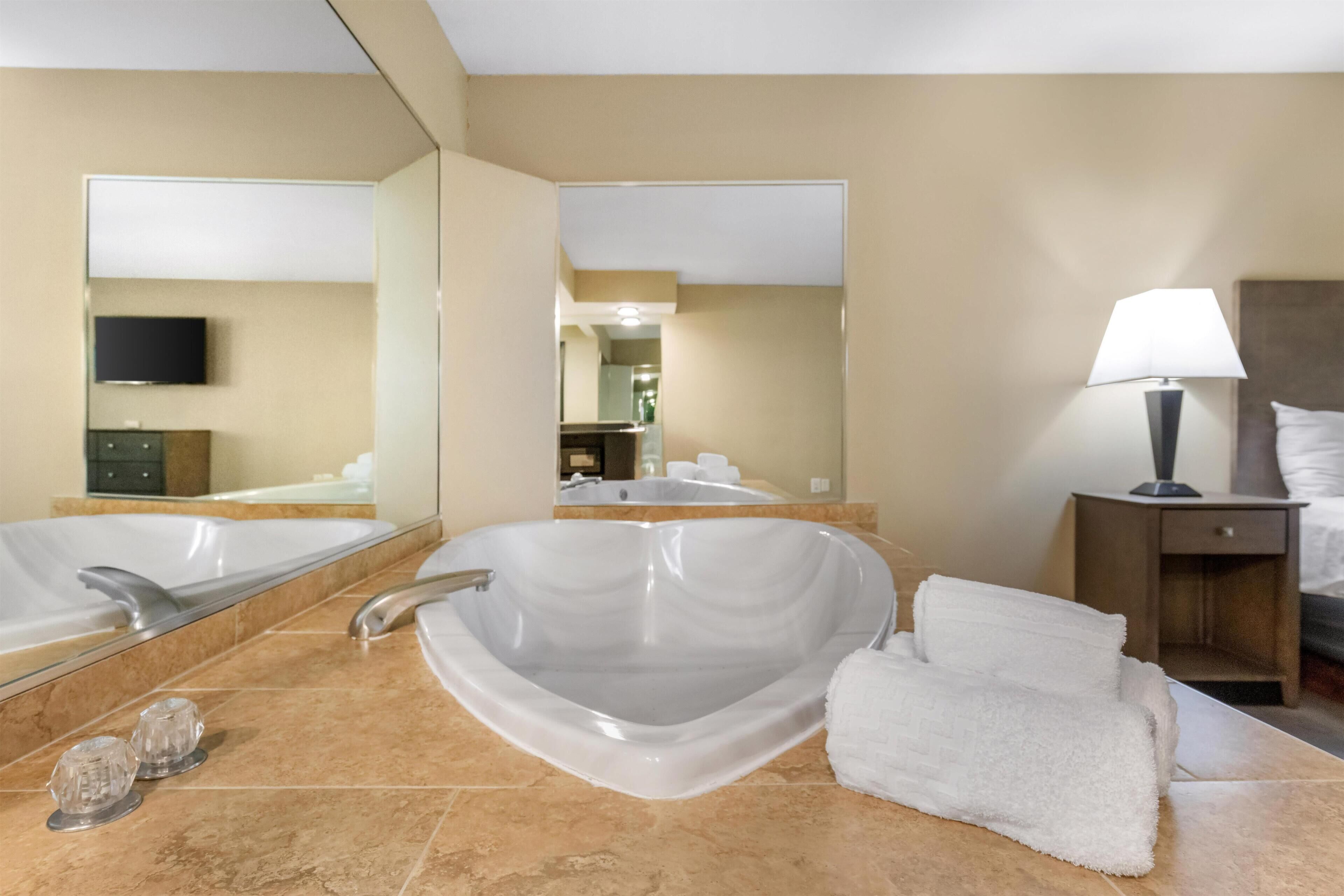 Ein modernes Badezimmer mit einer großzügigen, freistehenden Badewanne, einem Spiegel, einem Waschbecken und einem Nachttisch mit Lampe.