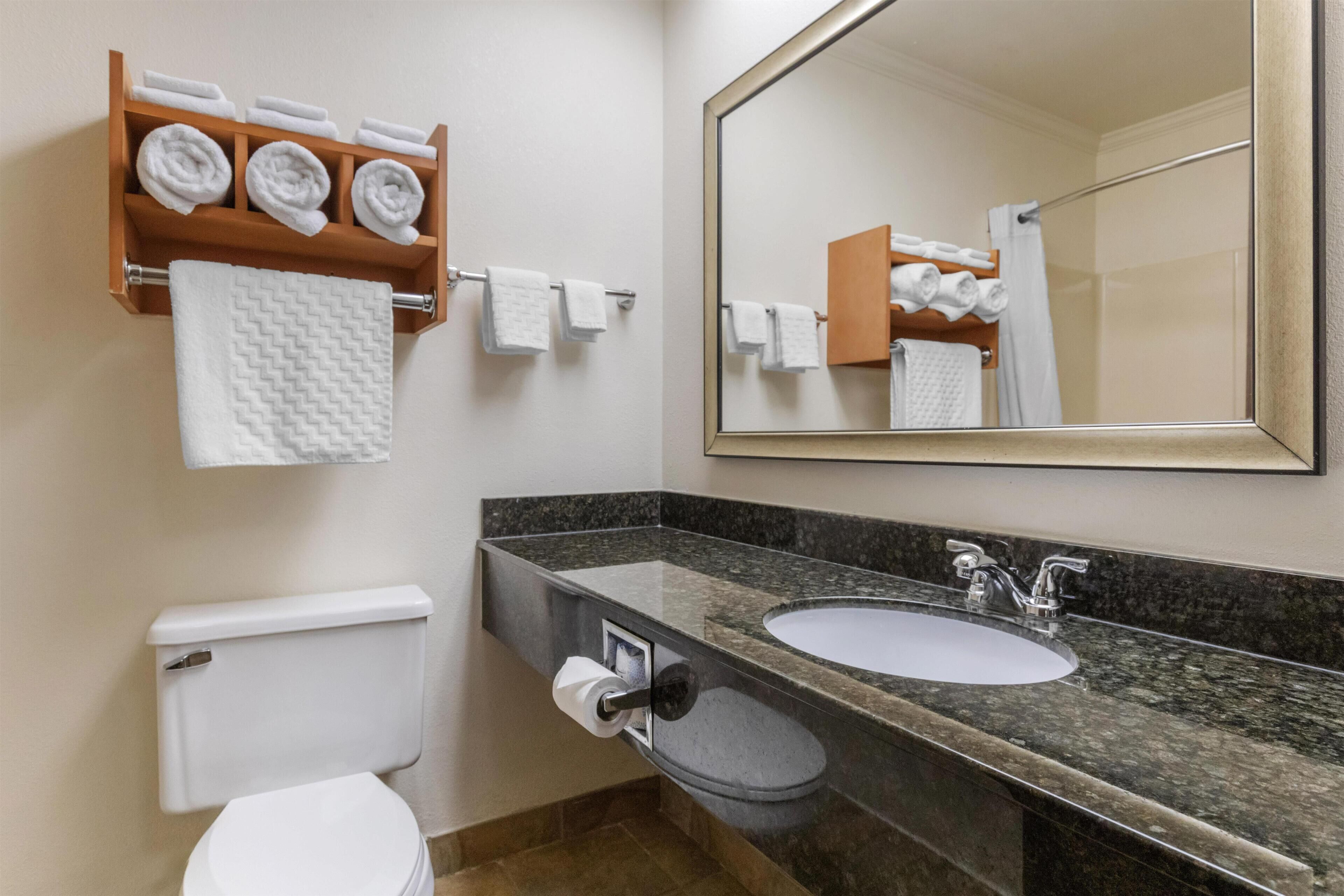 A bathroom with a toilet, sink, mirror, towel rack, and a wooden shelf with towels.