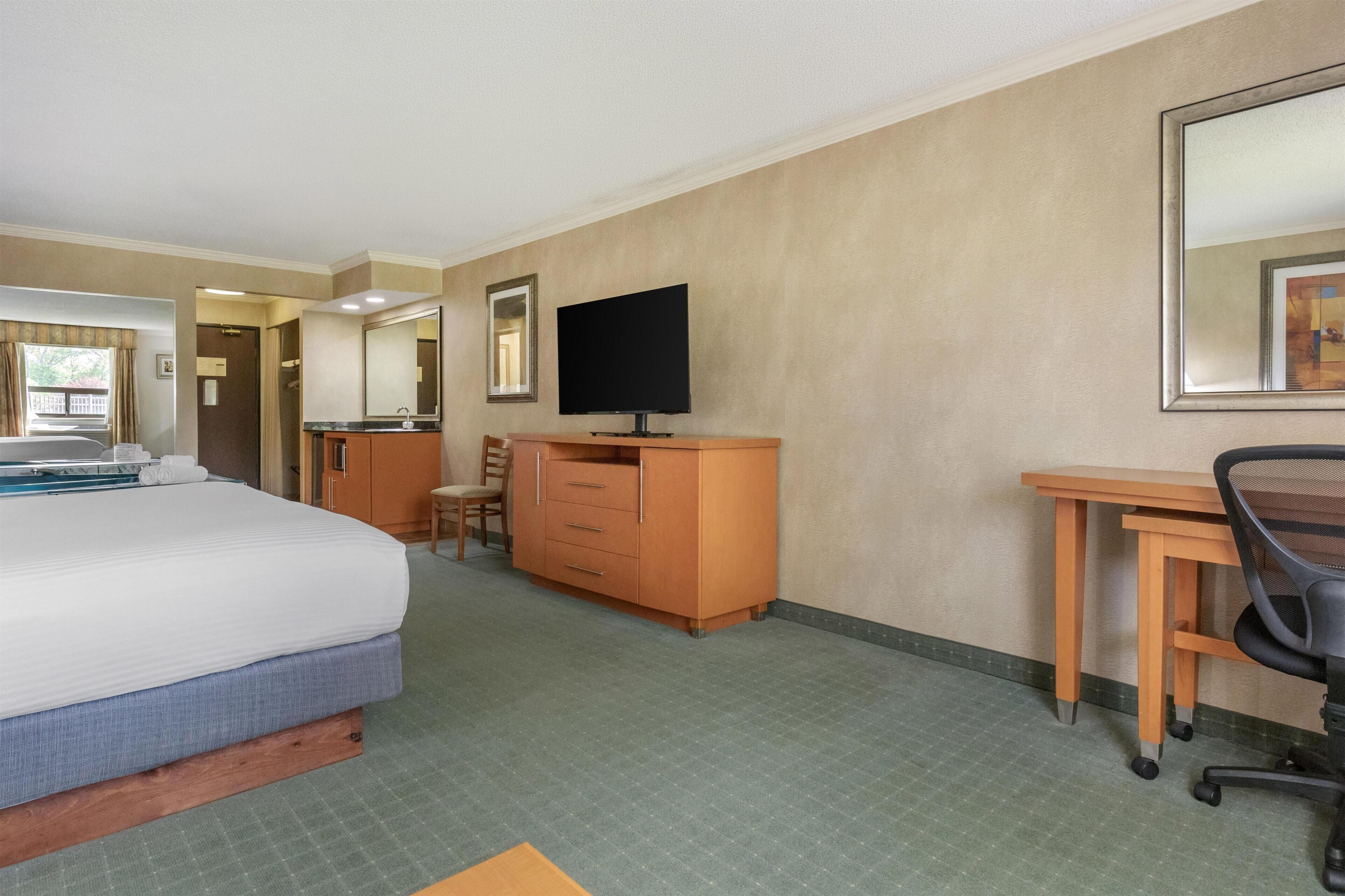 A hotel room with a bed, a desk, a chair, a TV, and a wardrobe.