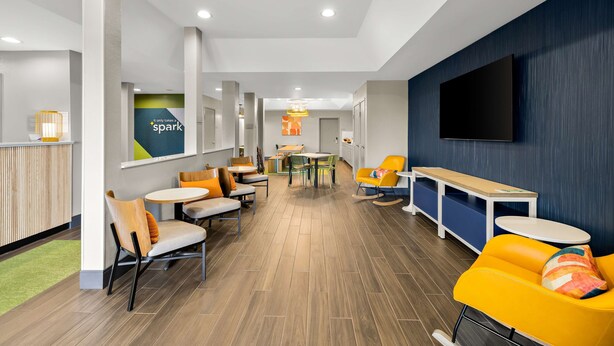 A modern hotel lobby with a wooden floor, yellow and orange seating, a large TV, and a 'spark' sign on the wall. - Spark by Hilton Tifton (Tifton)