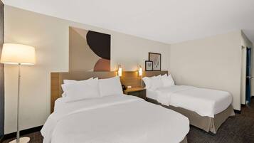 Habitación de hotel con dos camas, una mesita de noche con lámpara y una obra de arte en la pared.