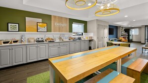 A modern kitchen with a wooden table and benches, a green accent wall, and a sign that reads "Delight in the day." - Spark by Hilton Tifton (Tifton)