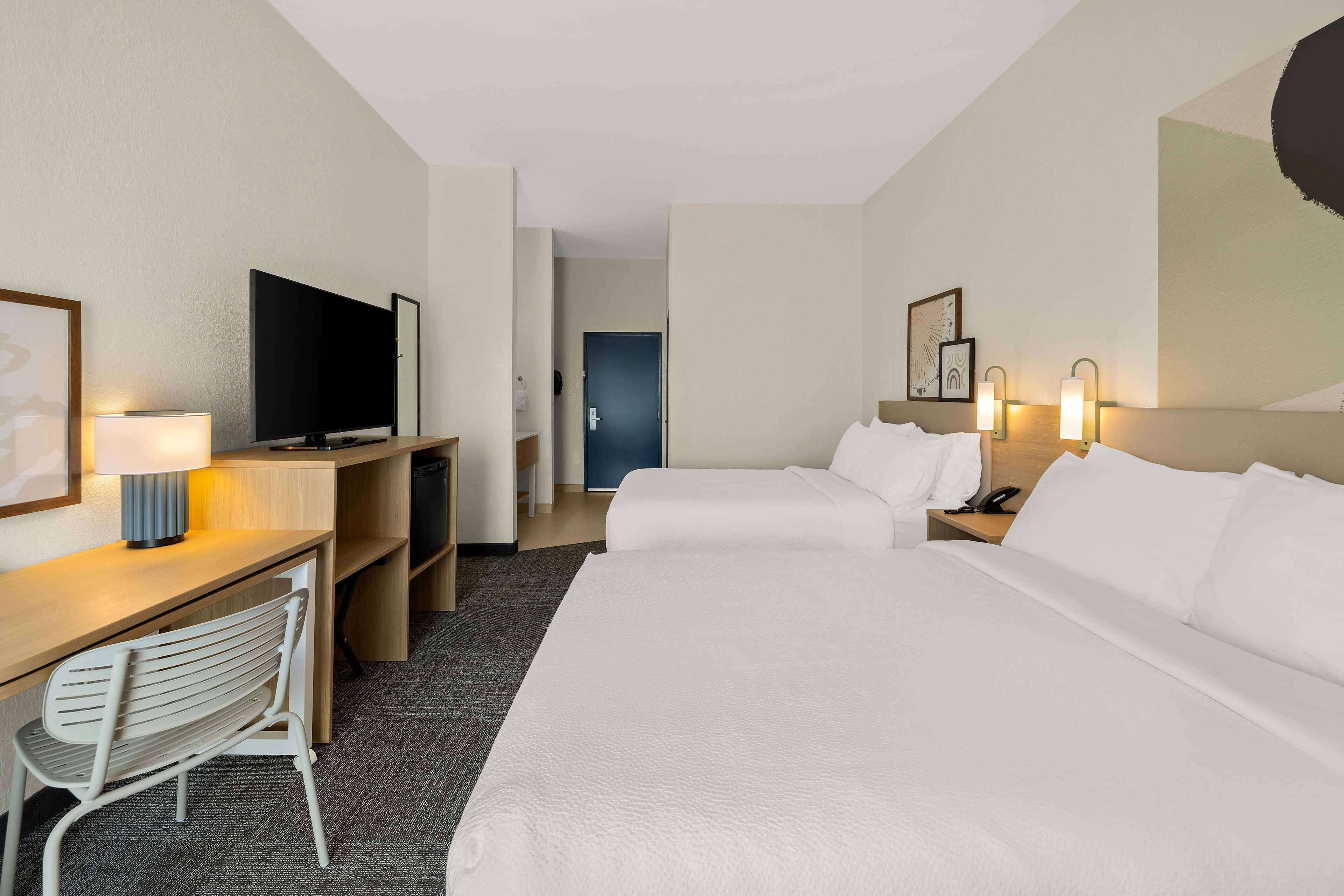 Ein Hotelzimmer mit zwei Betten, einem Schreibtisch mit Stuhl, einem Fernseher und einer Schreibtischlampe.