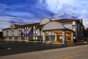 Un hotel moderno con entrada cubierta, varias ventanas y un estacionamiento.