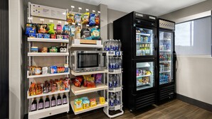 A self-service snack and beverage station with microwaves, refrigerators, and shelves stocked with snacks and drinks. - Spark by Hilton Tifton (Tifton)