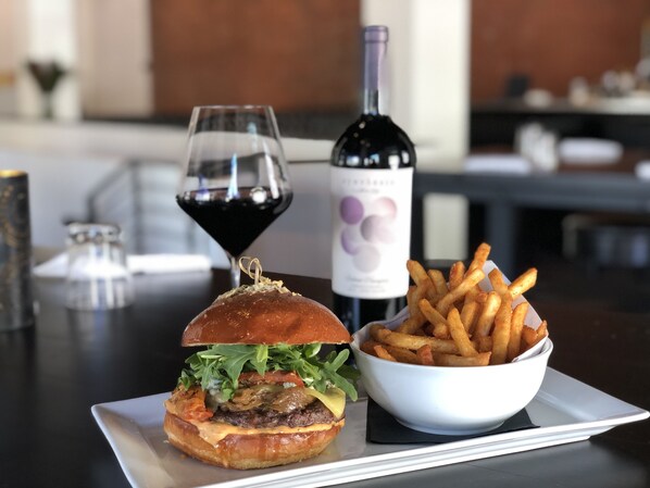 Una hamburguesa con papas fritas y una botella de vino sobre una mesa.